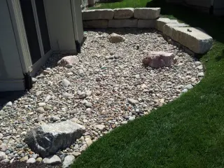 Cobblestone and river rock bed with accent boulders running along the foundation and lawn edge of a home